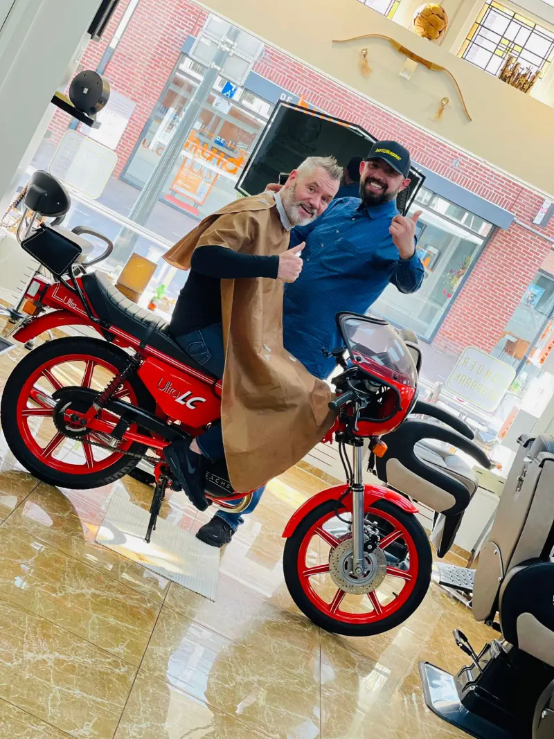 Kapper en klant steken hun duim op bij de rode brommer in de salon