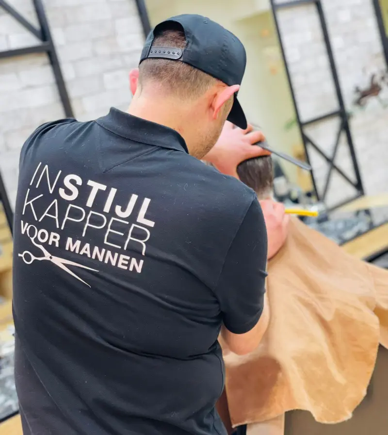 Kapper van InStijl Kapper knipt een klant; op de rug van zijn zwarte polo staat het logo InStijl Kapper voor mannen
