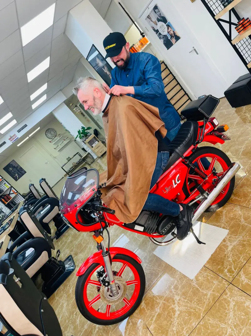 Klant wordt geknipt terwijl hij op een rode brommer in de salon zit