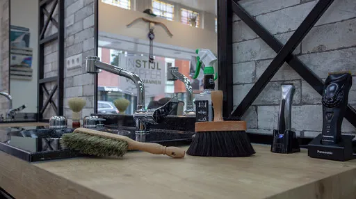 Interieur van de salon: kappersstoelen voor spiegels met zwarte stalen frames langs een witte bakstenen wand